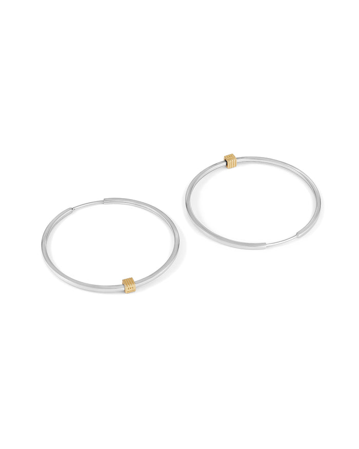 A pair of rhodium-plated medium-sized hoop earrings with a single engraved cube detail on one side.