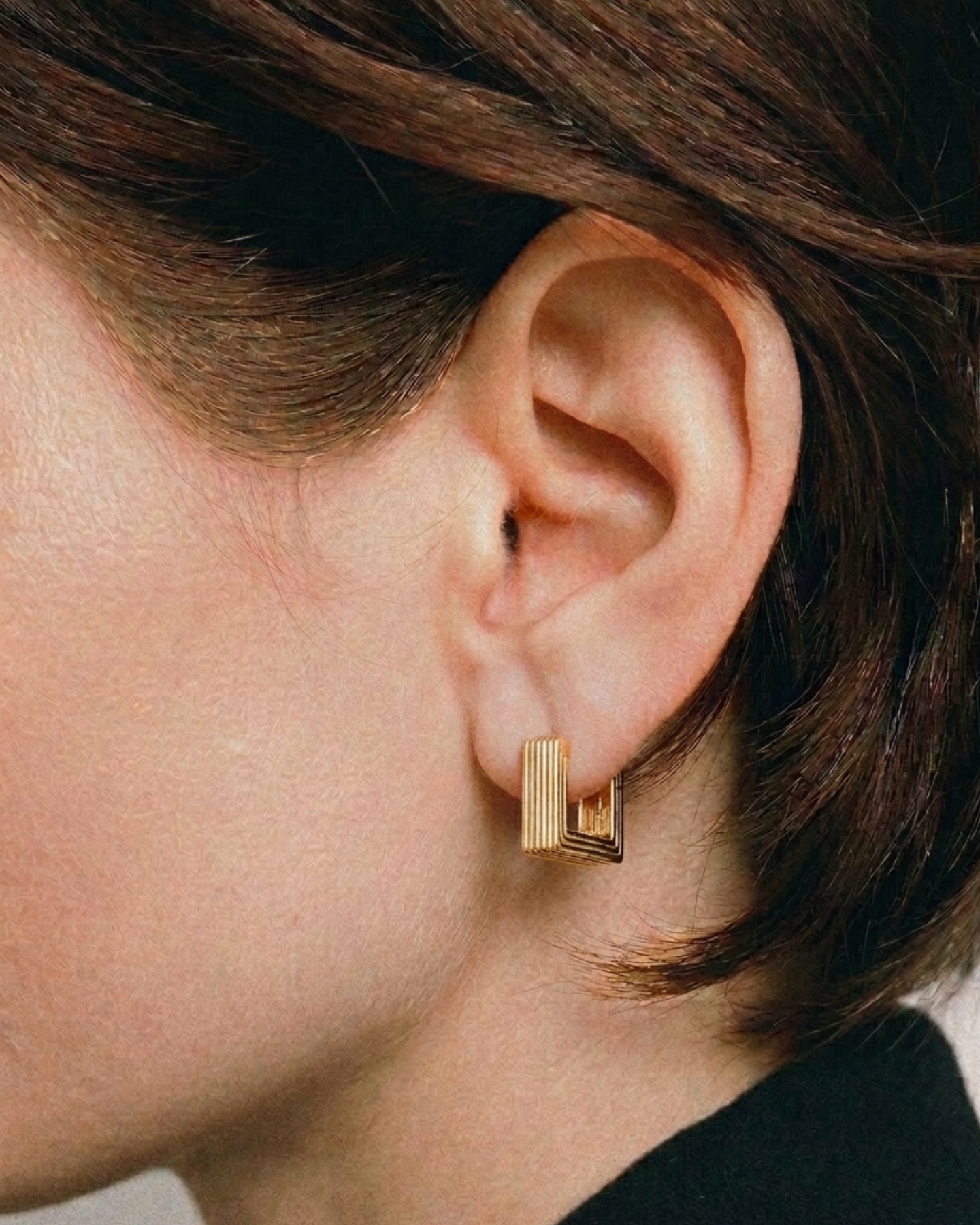 Pair of gold-plated Mini Aurelia sculptural square hoop earrings worn by a model. 