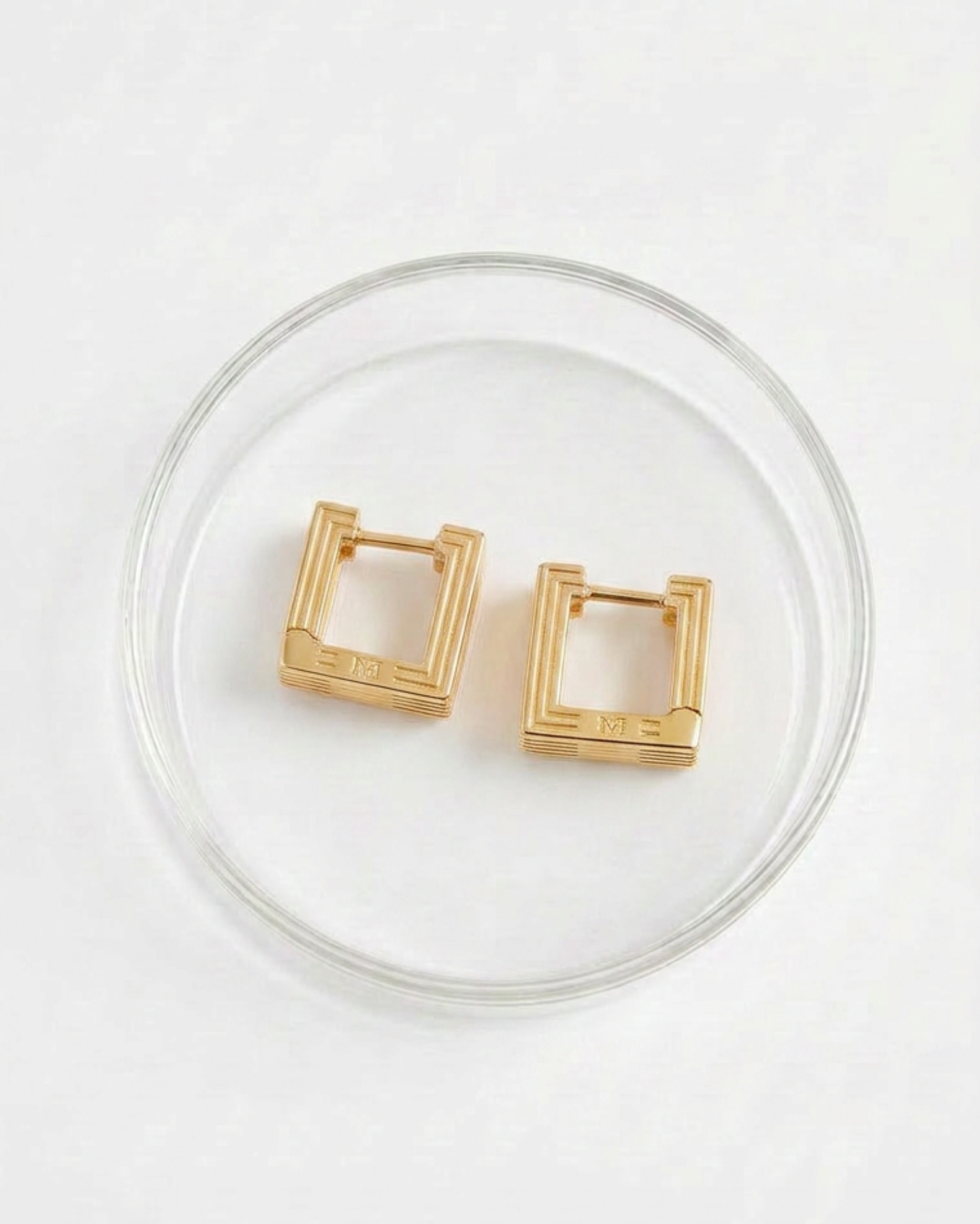 Pair of gold-plated Mini Aurelia sculptural square hoop earrings placed in glass packaging. 