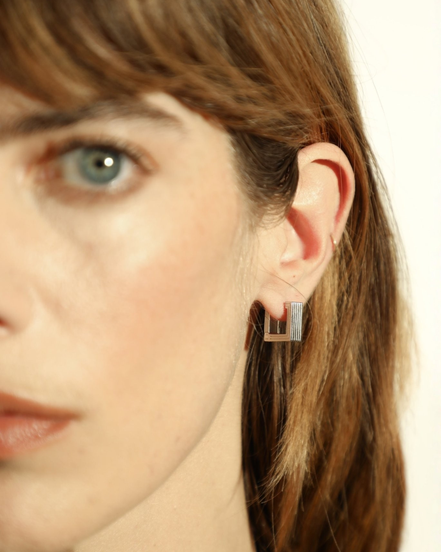 Pair of rhodium-plated Mini Aurelia sculptural square hoop earrings worn by a model. 