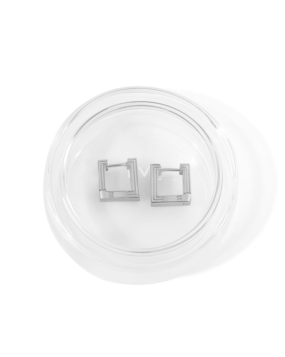 Pair of rhodium-plated Mini Aurelia sculptural square hoop earrings placed in glass packaging. 