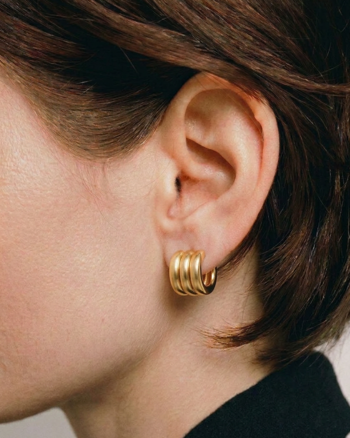 Pair of gold-plated Mini Gaia sculptural hoop earrings worn by a model. 