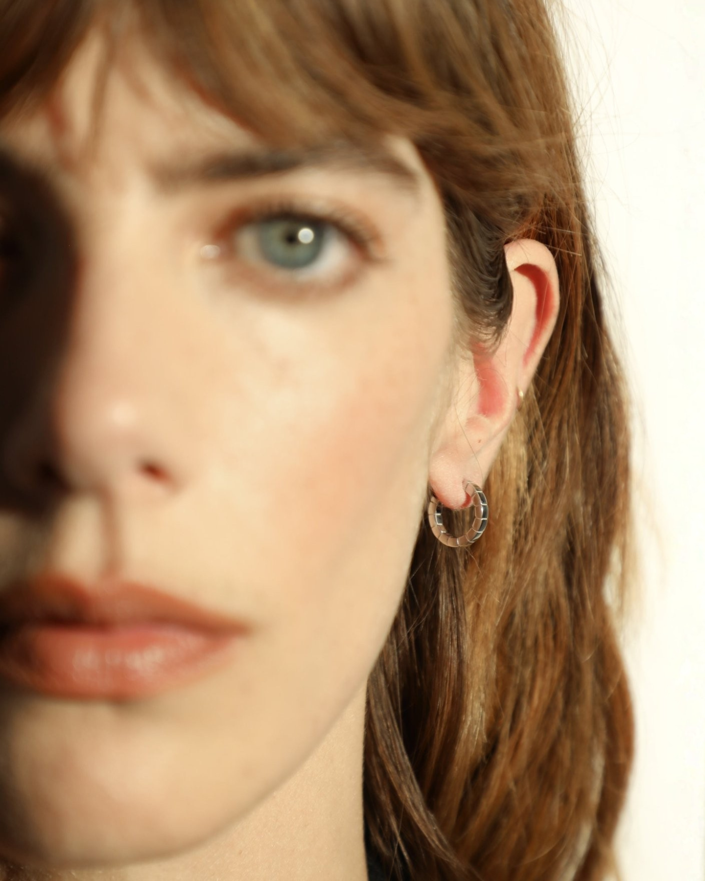 A pair of mini rhodium-plated Signore hoop earrings with a textured design, resembling a curving row of square beads worn by a model. 