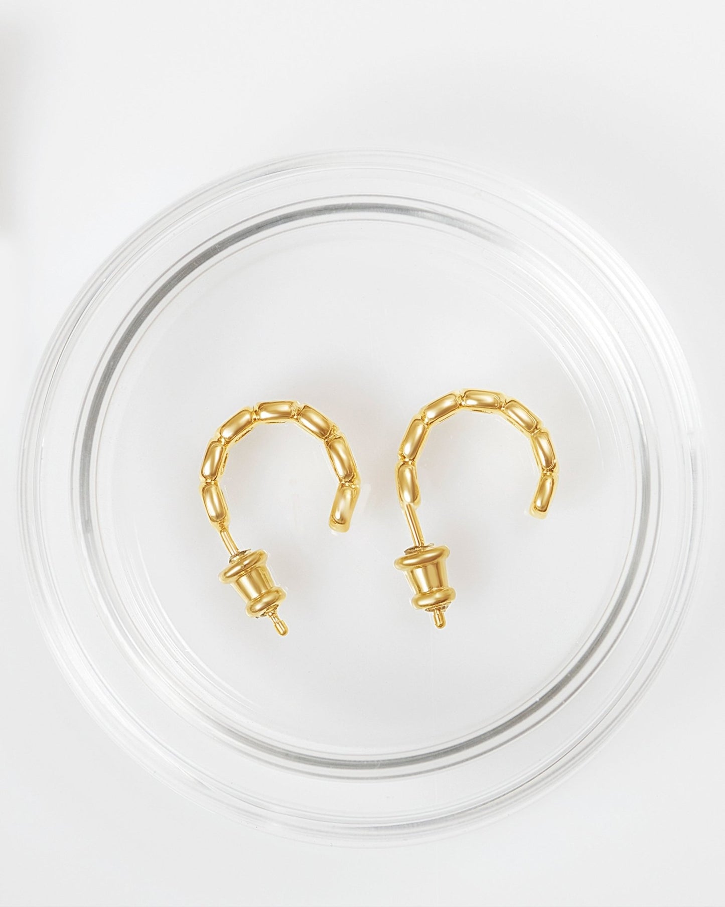 A pair of gold-plated mini toy hoop earrings with oval links in glass packaging. 