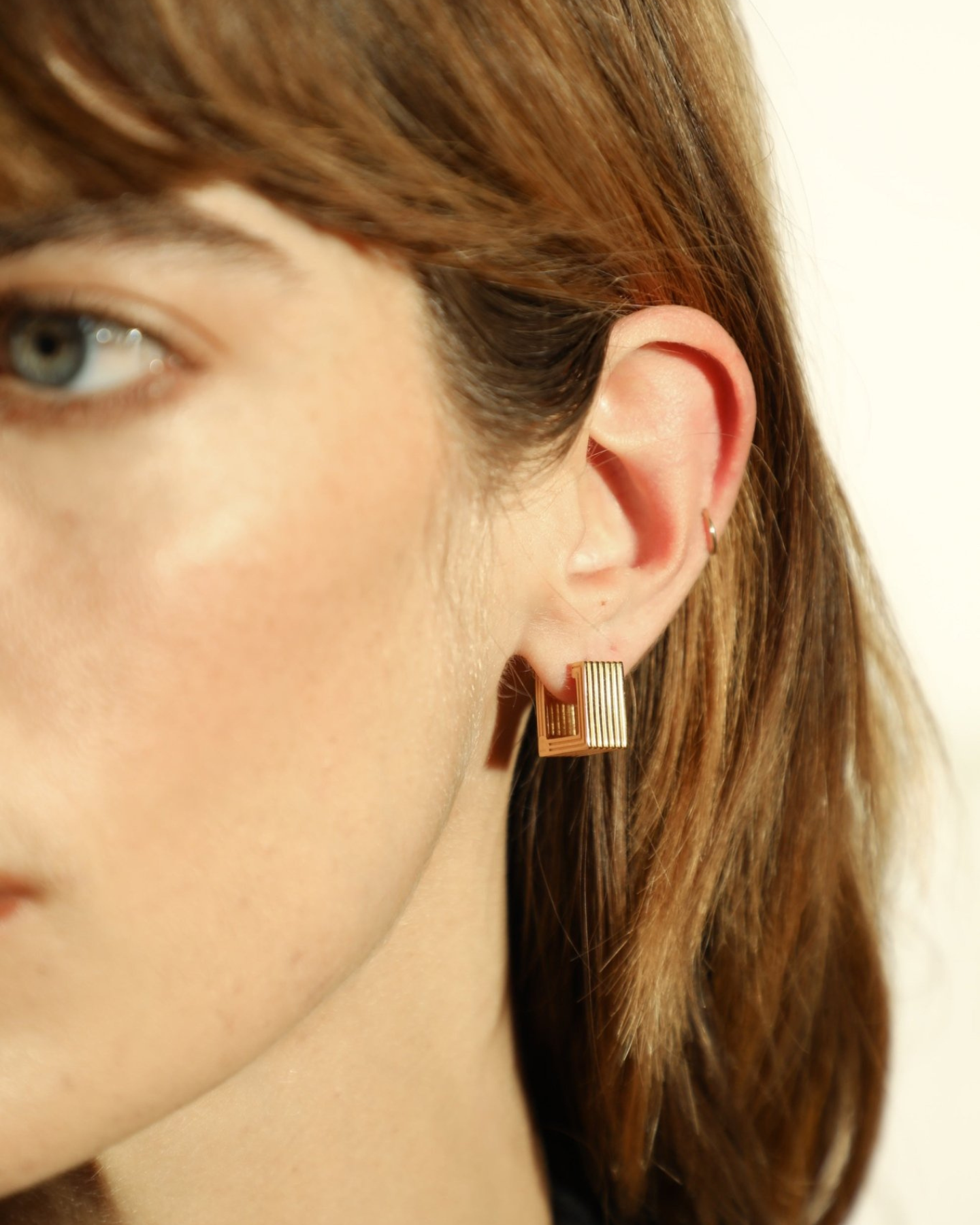 Pair of gold-plated Mini Wide Aurelia sculptural square hoop earrings worn by a model. 