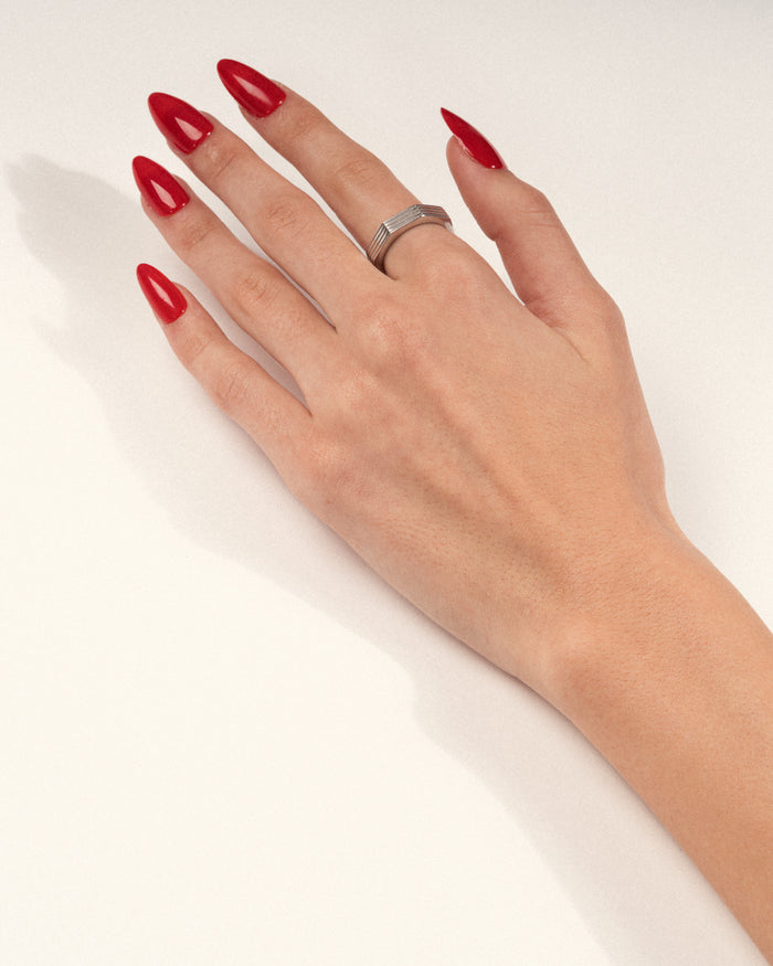 Hexagonal rhodium-plated ring worn on a hand with red nails, shown in a lifestyle close-up.
