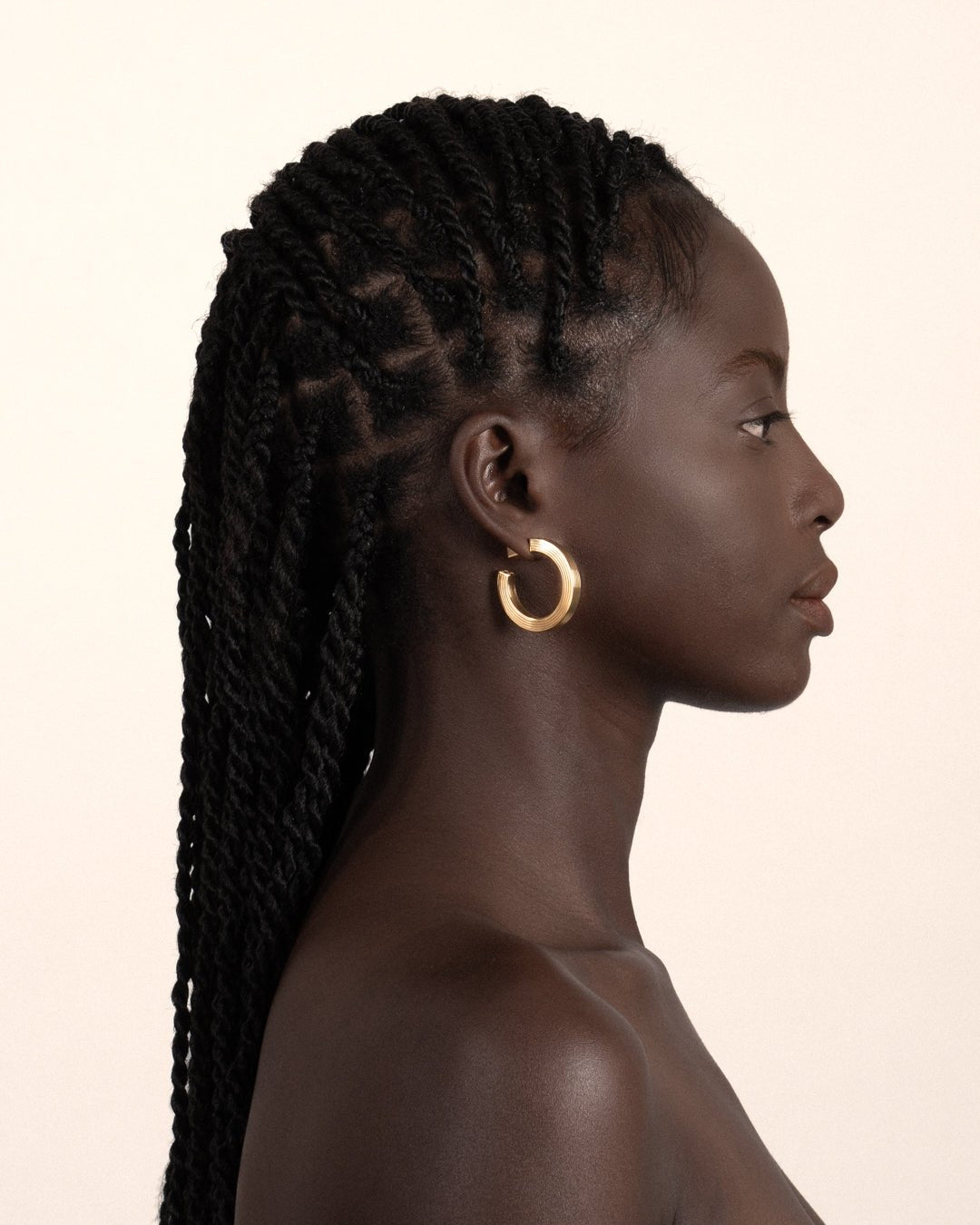 A pair of gold-plated hollow hoop earrings with a square post worn by a model. 