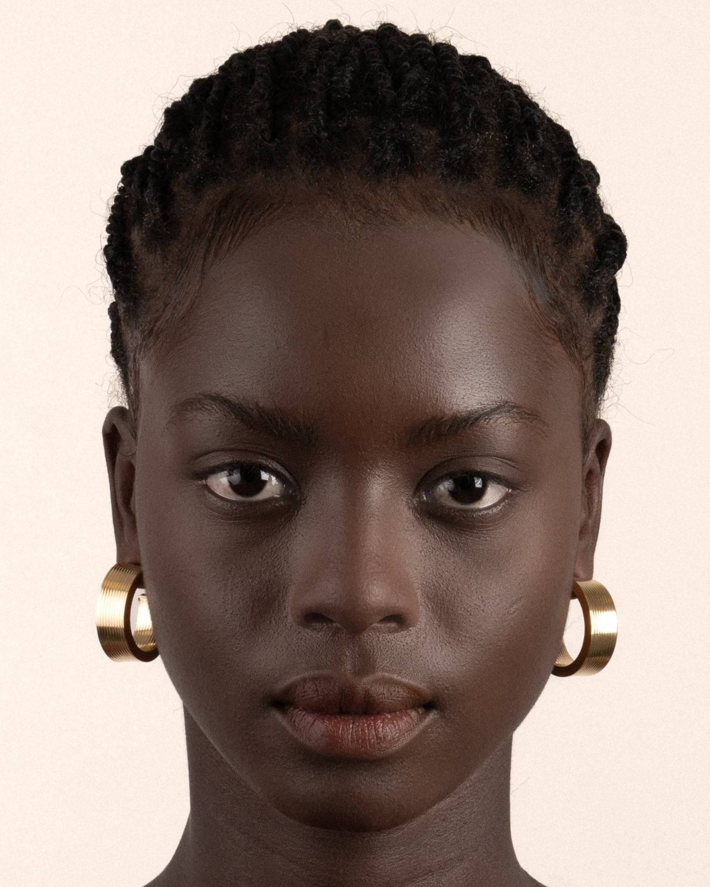 A pair of gold-plated hollow hoop earrings with a square post, worn by a model. 