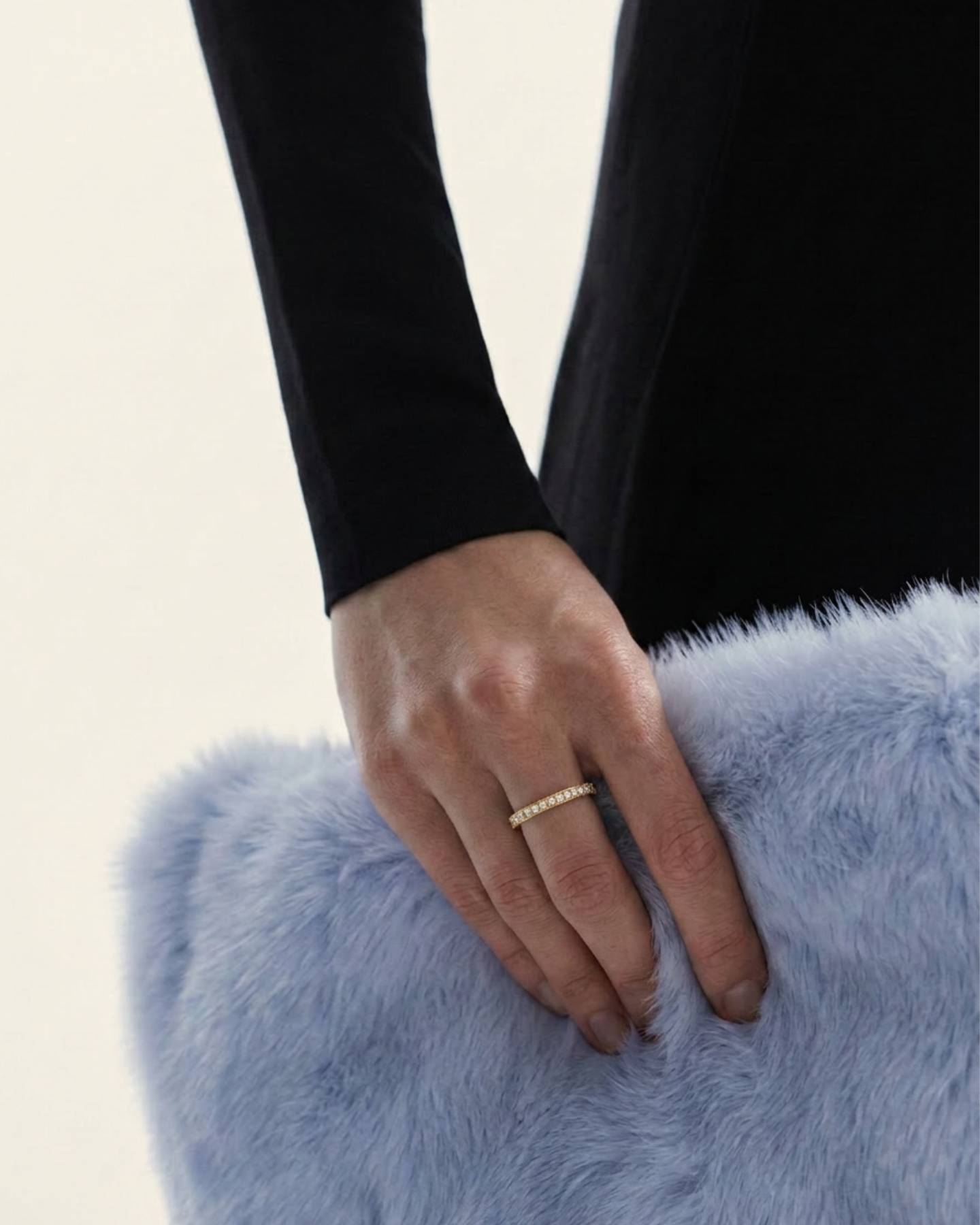 An 18-karat gold band ring with round-cut diamonds on a light blue fluffy surface.