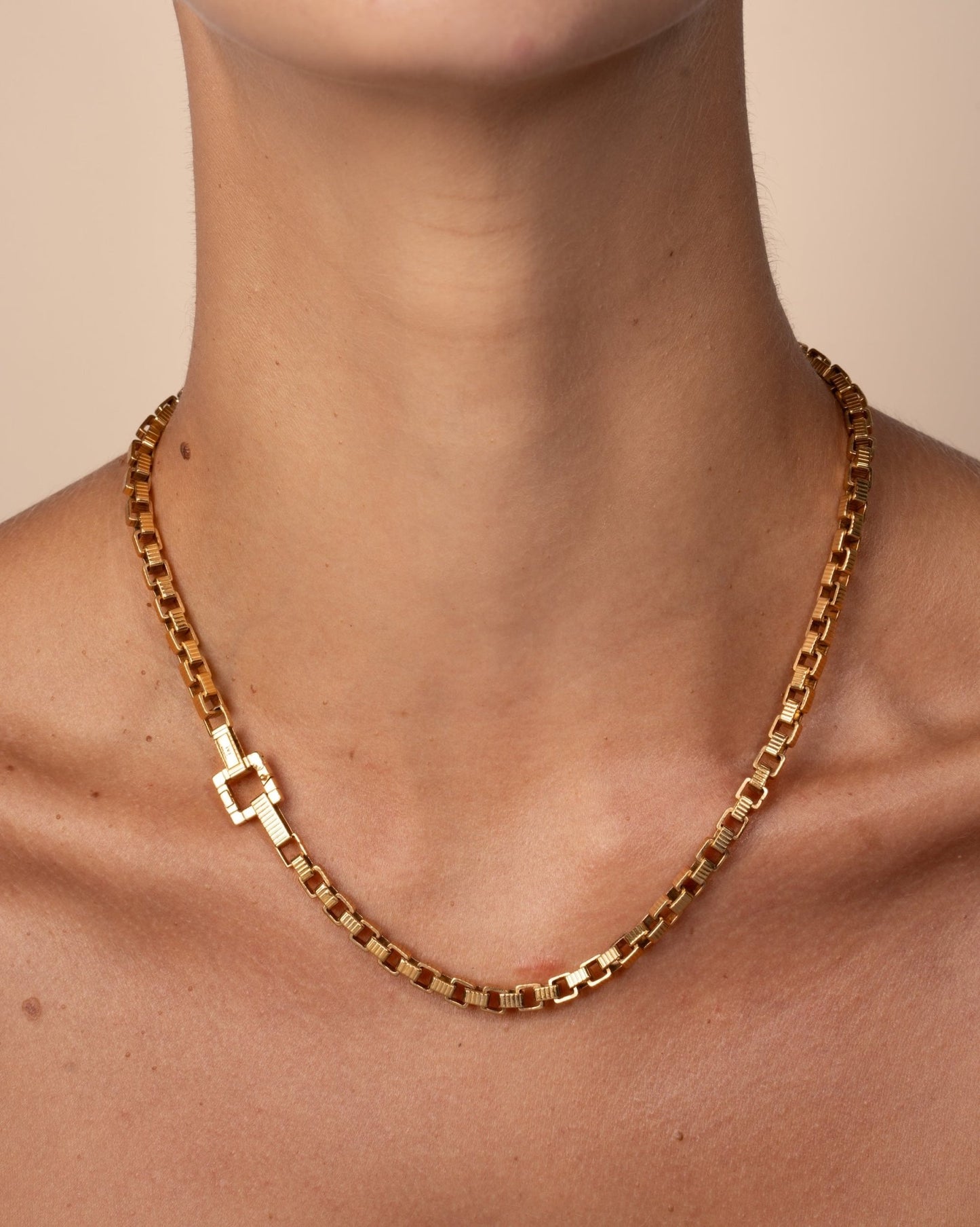 A gold-plated chain necklace with a square clasp, worn on a model. 
