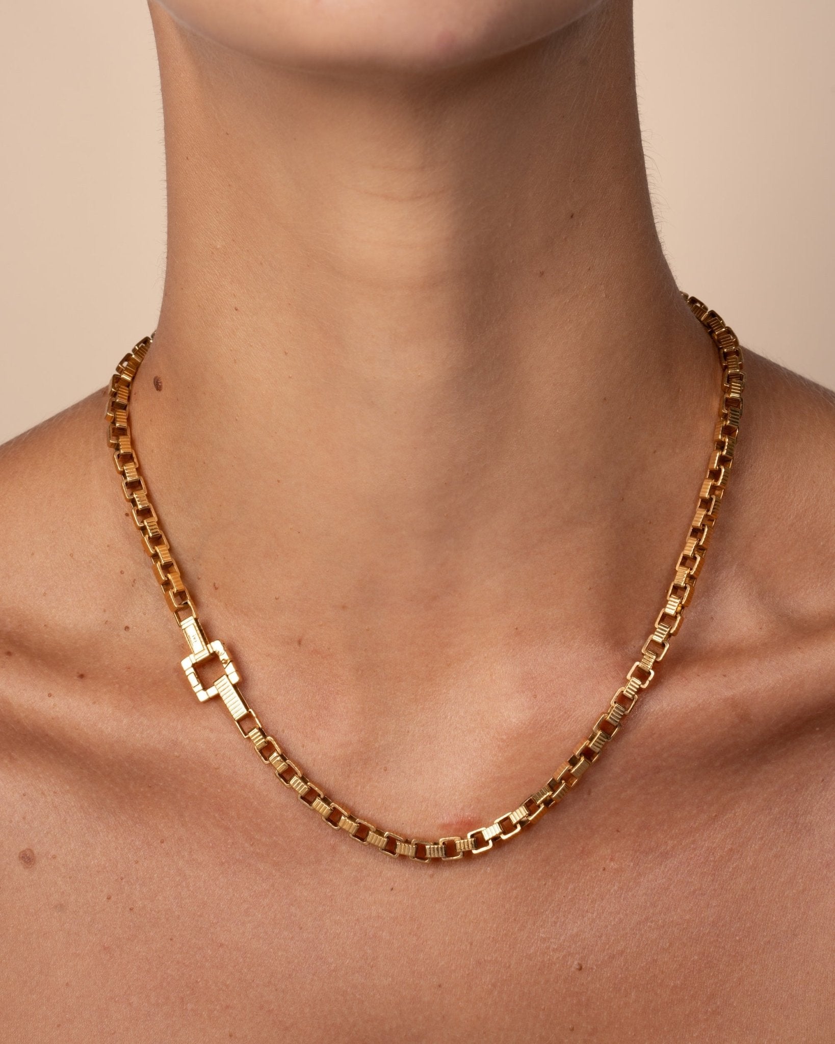 A gold-plated chain necklace with a square clasp, worn on a model. 