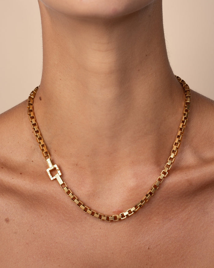 A gold-plated chain necklace with a square clasp, worn on a model. 