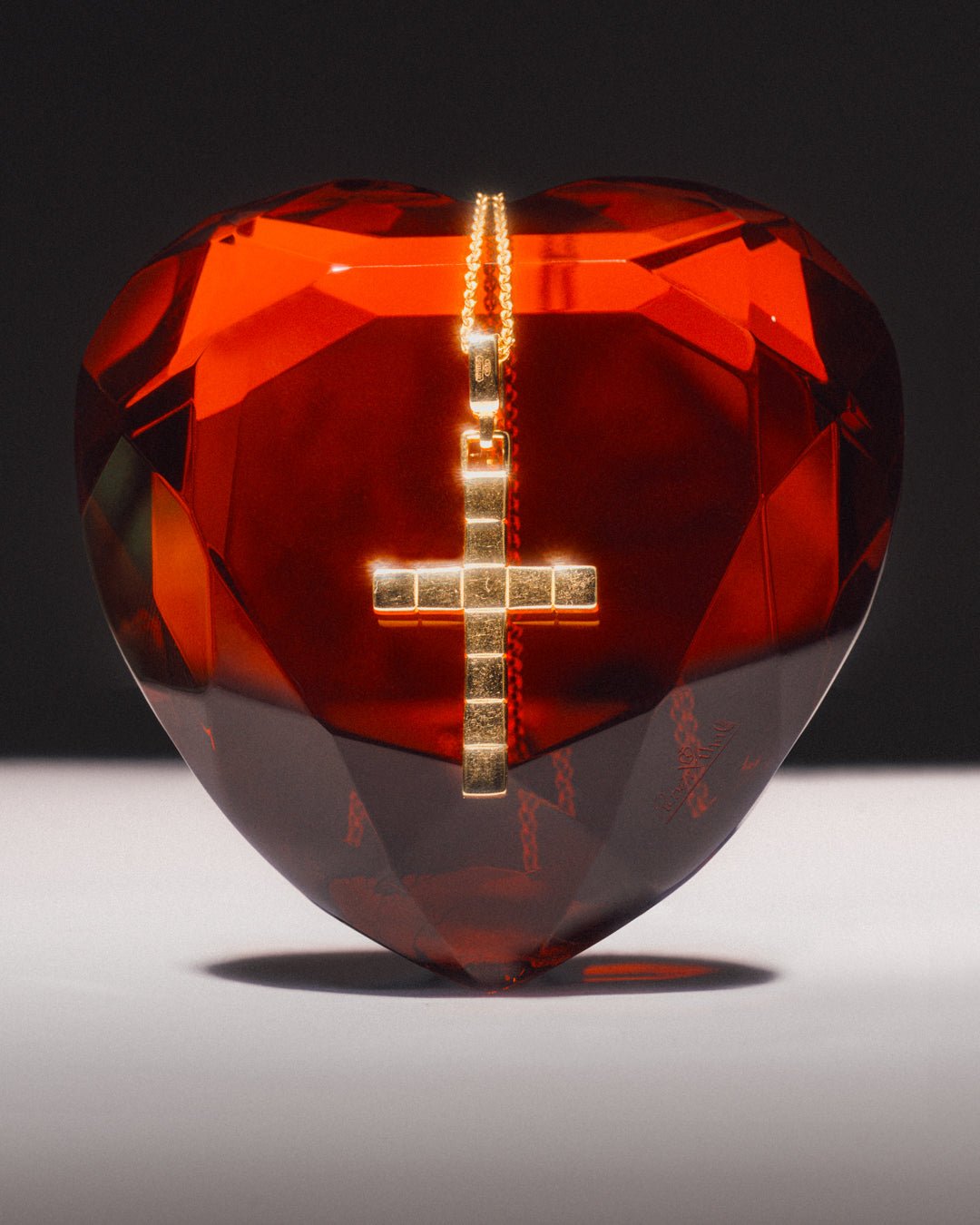 A gold-plated cross necklace with a custom chain, displayed draped over a red faceted heart.