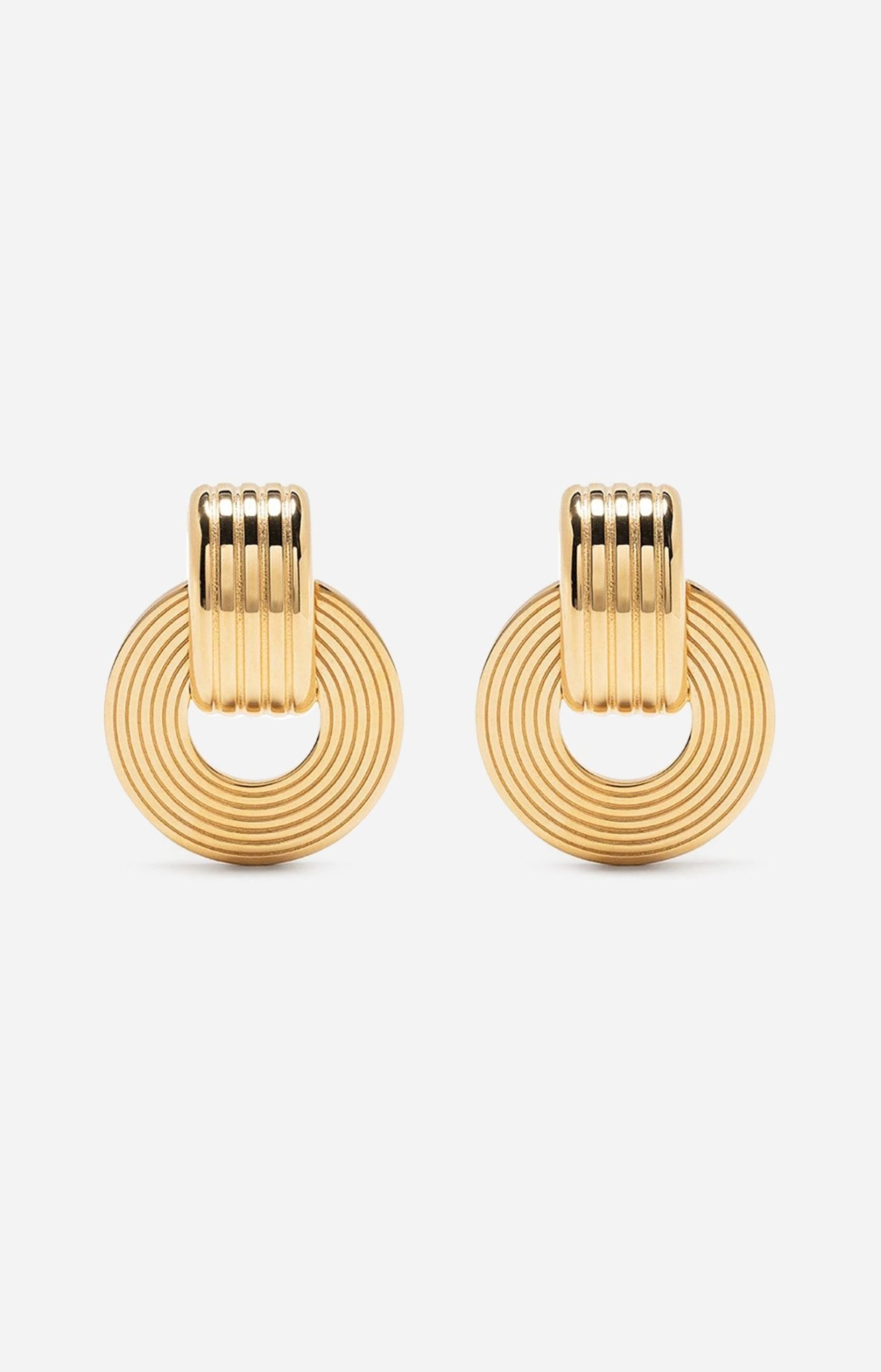 A pair of gold-plated oval hoop earrings with a circular pendant attached to the hoop, featuring intricate engravings.