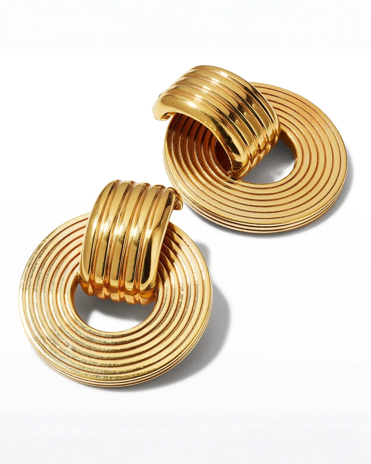 A pair of gold-plated oval hoop earrings with a circular pendant attached to the hoop, featuring intricate engravings.