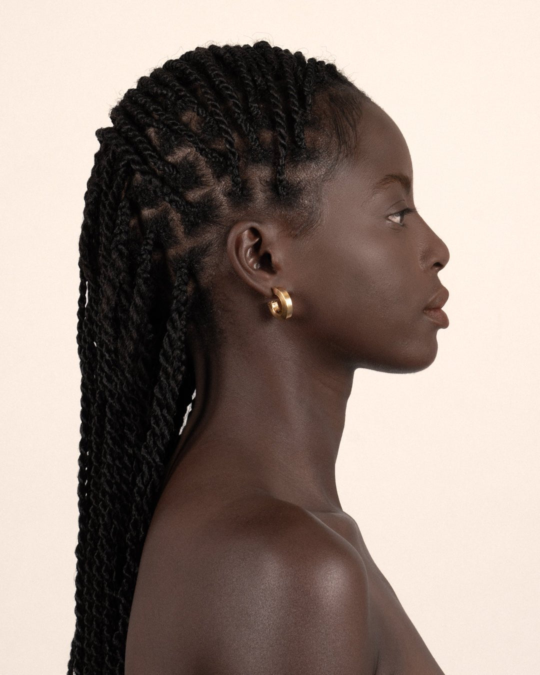A pair of gold-plated hollow hoop earrings with a square post worn by a model. 