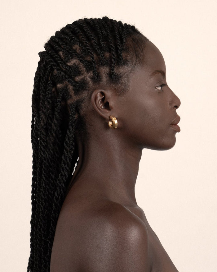 A pair of gold-plated hollow hoop earrings with a square post worn by a model. 