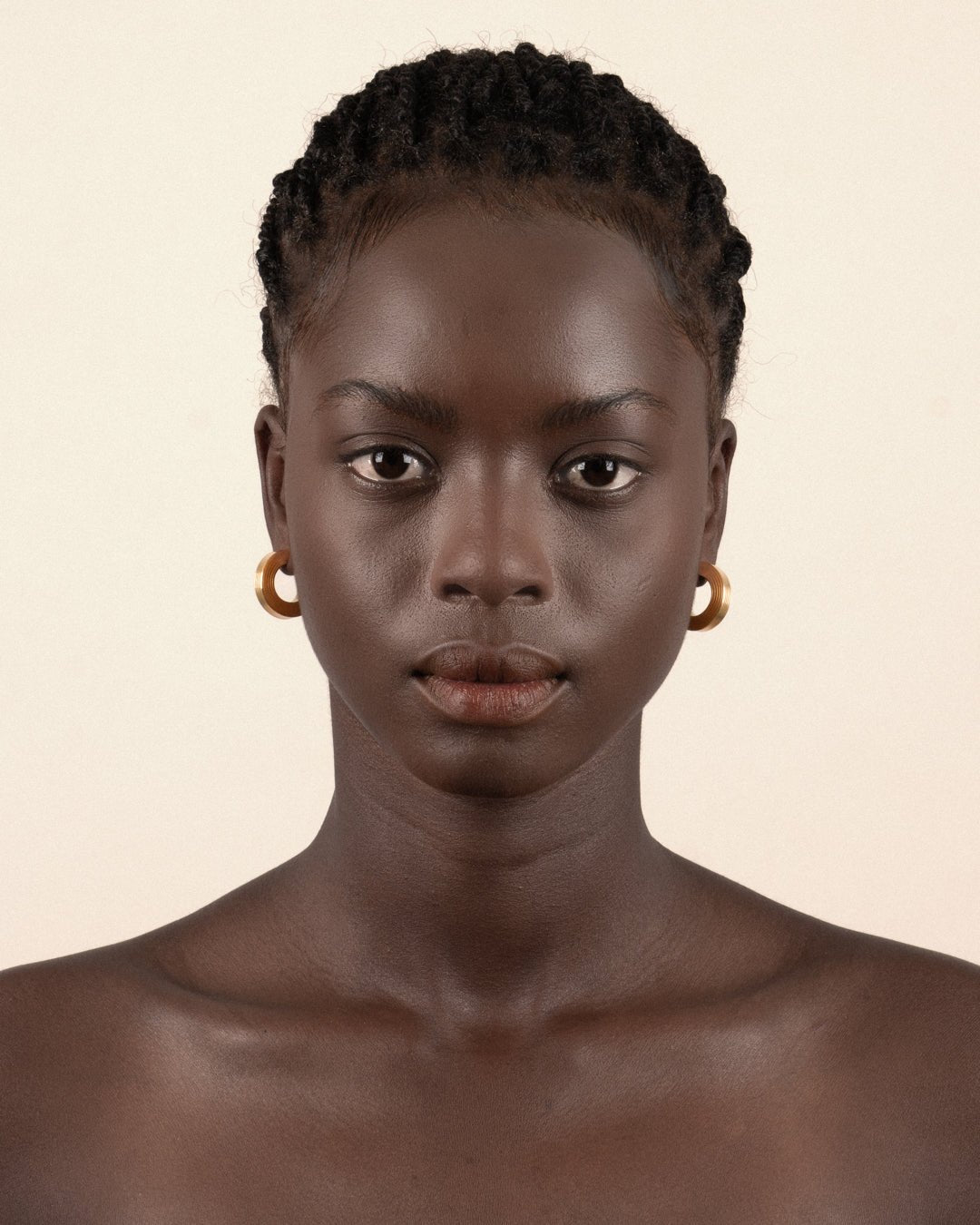 A pair of gold-plated hollow hoop earrings with a square post worn by a model. 