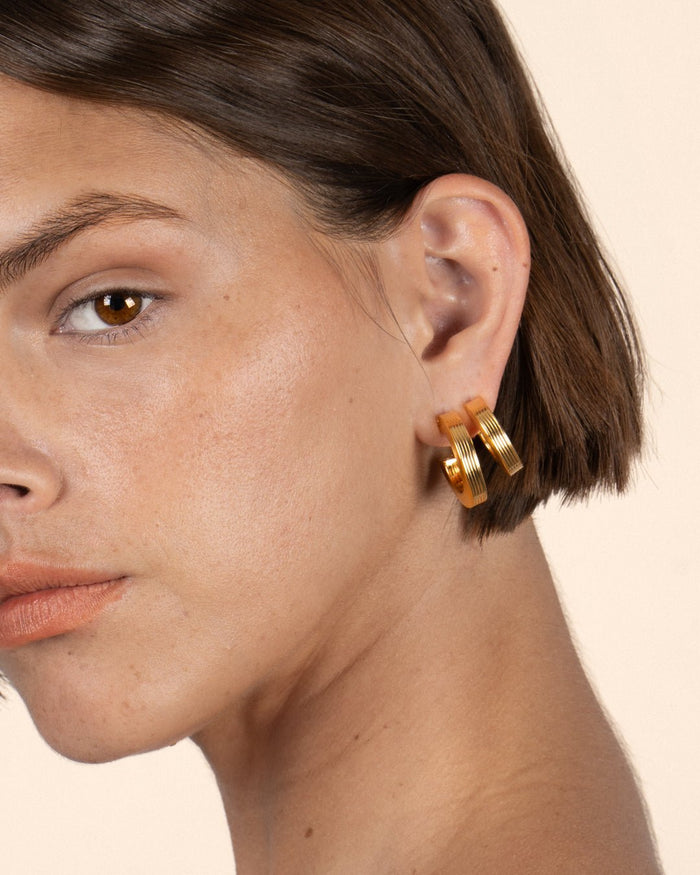 A pair of gold-plated hoop earrings with a square post, worn by a model. 