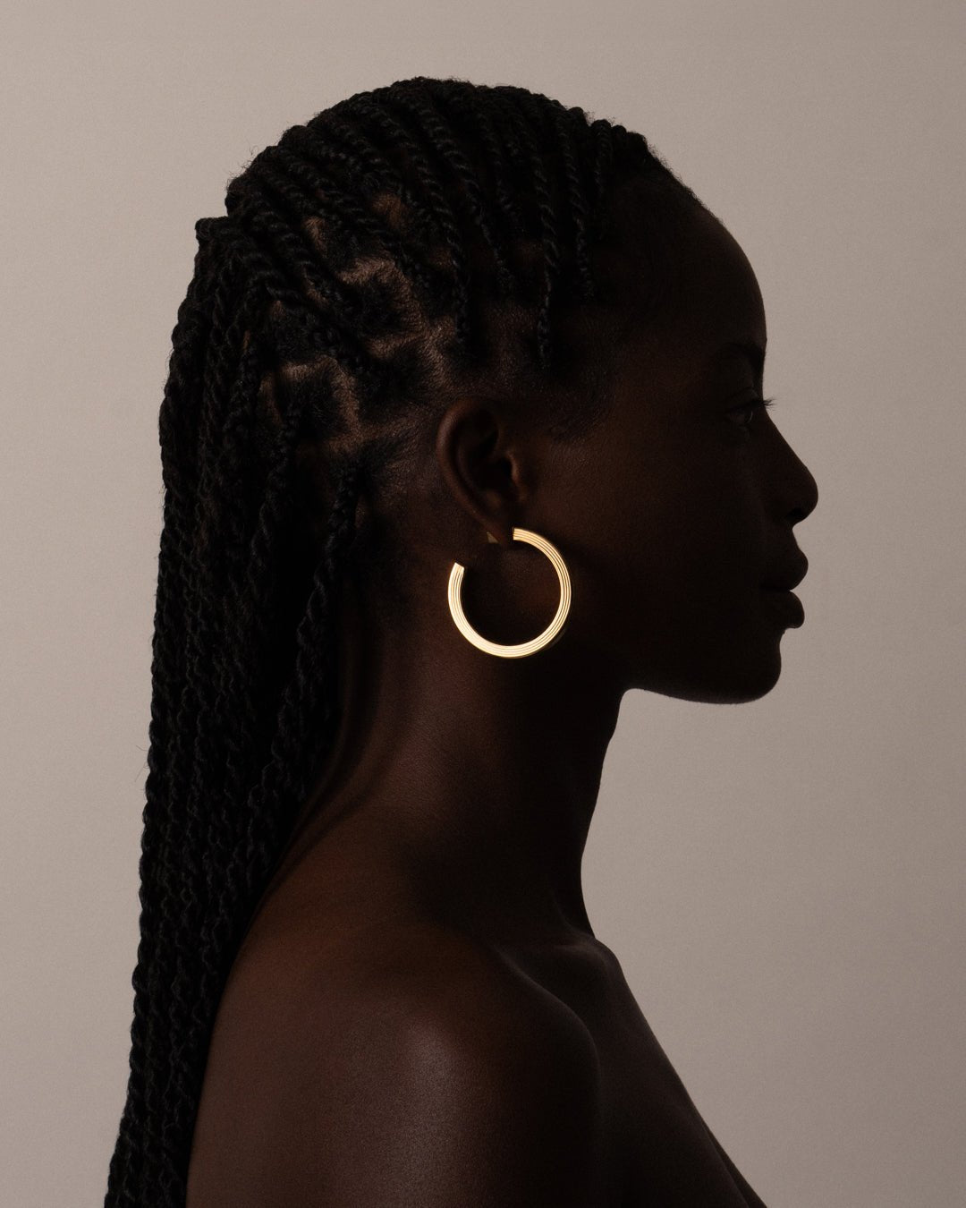 A pair of gold-plated hoop earrings with a square post, worn by a model. 