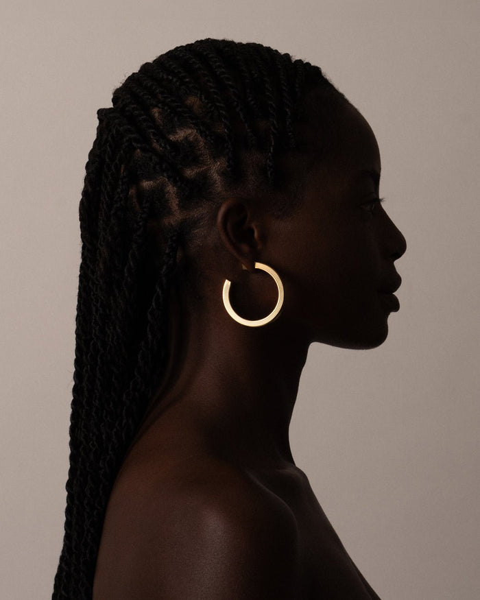 A pair of gold-plated hoop earrings with a square post, worn by a model. 