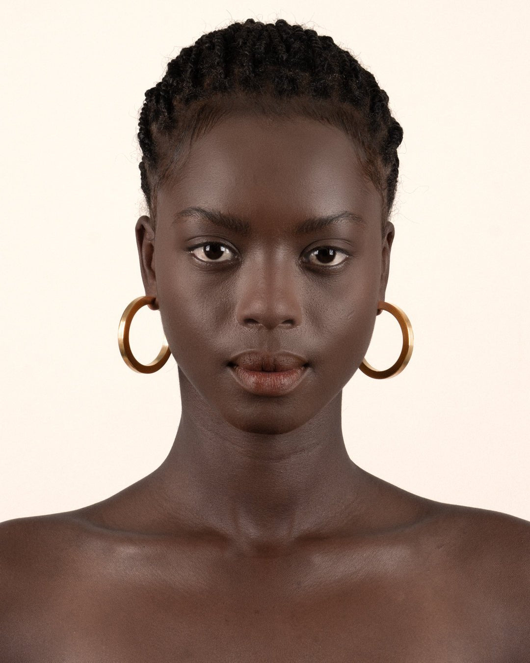 A pair of gold-plated hoop earrings with a square post, worn by a model. 
