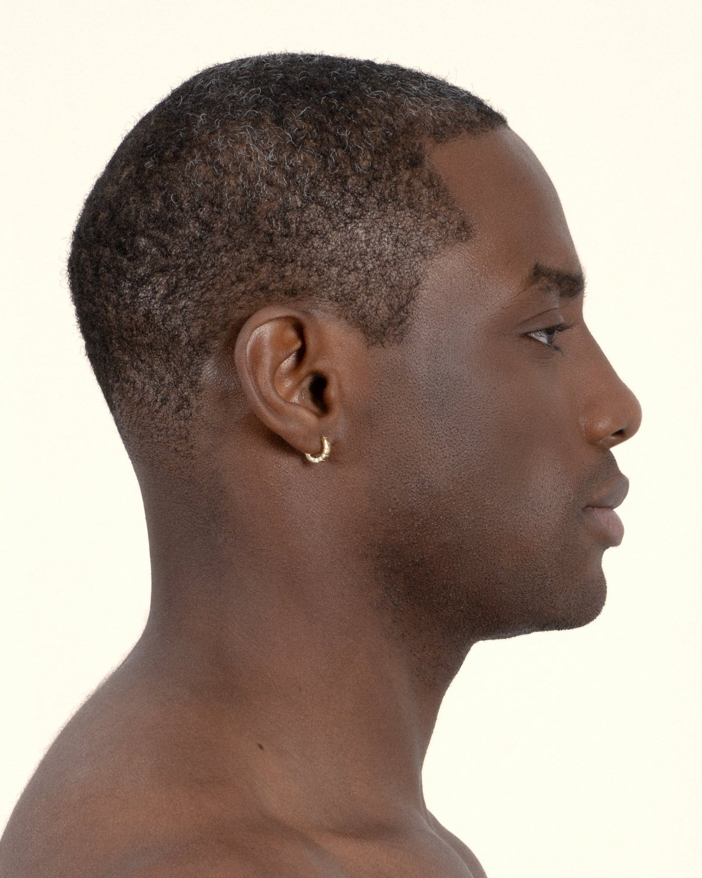 A pair of mini gold-plated Signore huggies with a textured design, resembling a curving row of square beads, worn by a model. 