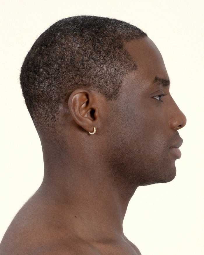 A pair of mini gold-plated Signore huggies with a textured design, resembling a curving row of square beads, worn by a model. 