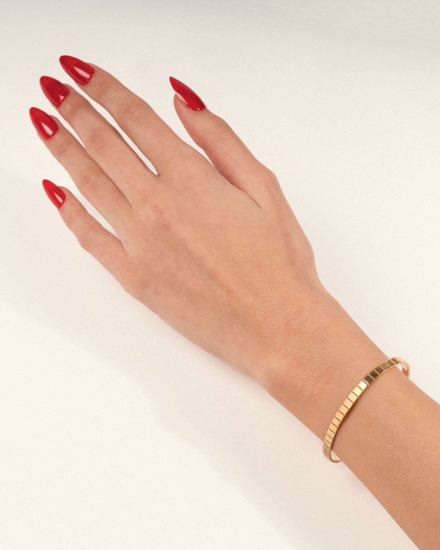 A gold-plated single slot cuff bracelet with a grooved profile worn on a hand with red nails, shown in a lifestyle close-up.