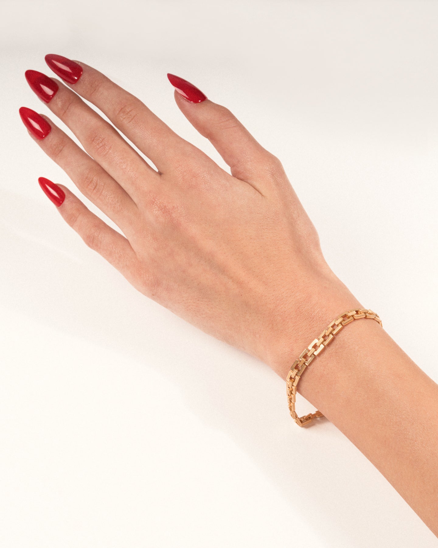 A gold-plated Aurelia Chain bracelet with interlocking square links worn on a hand with red nails, shown in a lifestyle close-up.