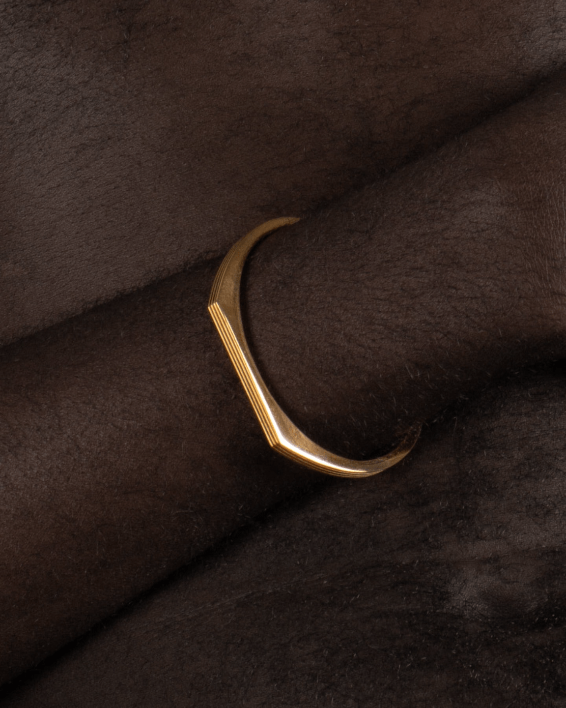 A gold-plated cuff bracelet with a sleek, modern design worn by a model. 