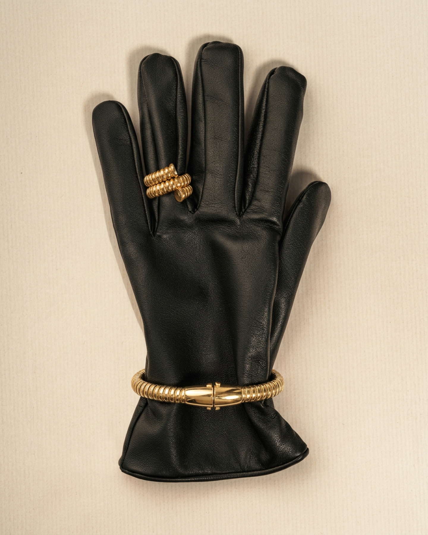 Gold-plated tubogas bracelet with a flexible ribbed design and concealed clasp placed on a black leather glove. 