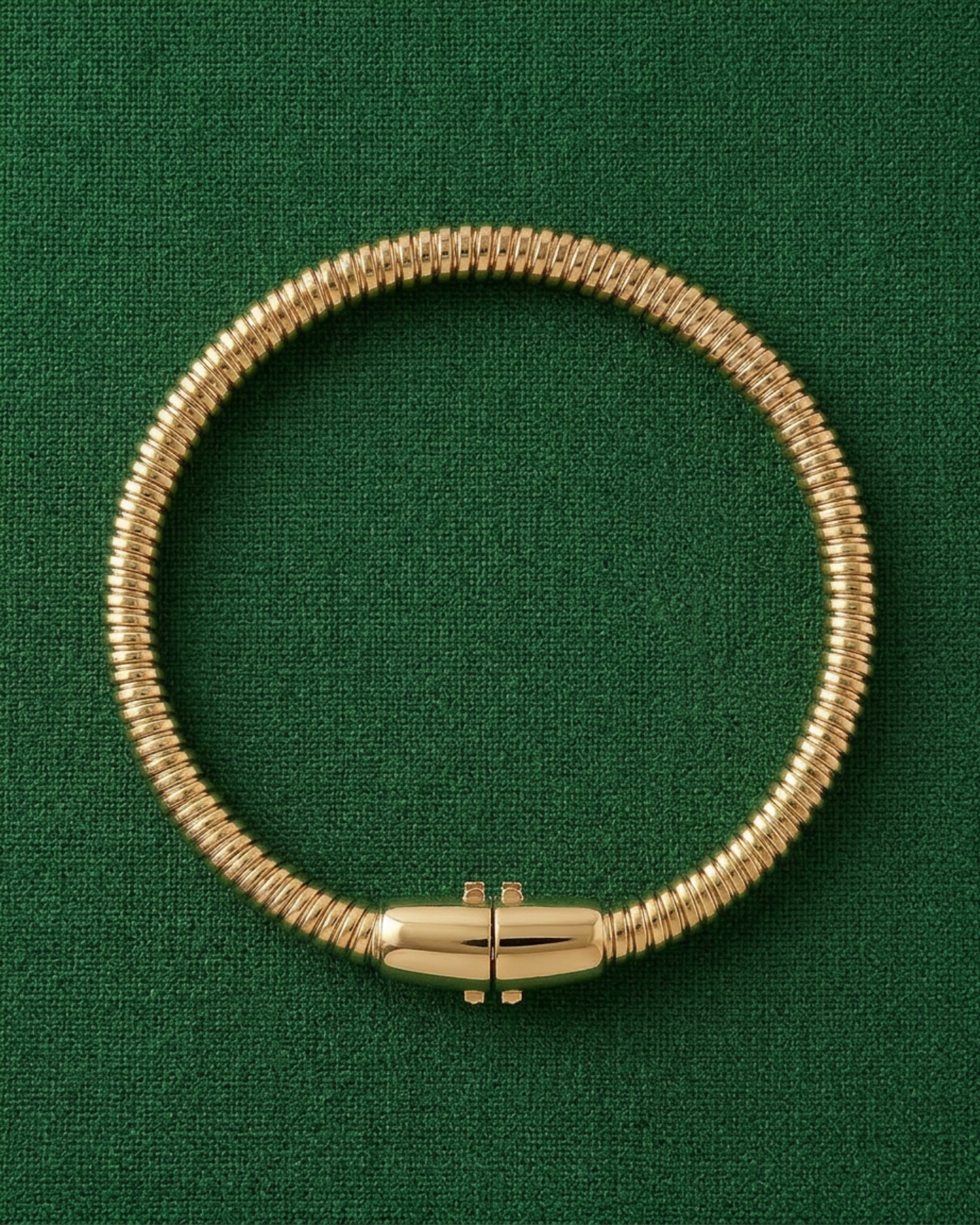 Gold-plated tubogas bracelet with a flexible ribbed design and concealed clasp on a green background.