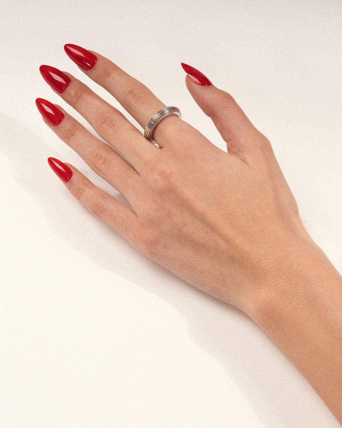 A rhodium-plated, round-shaped ring with linear engravings worn on a hand with red nails, shown in a lifestyle close-up.