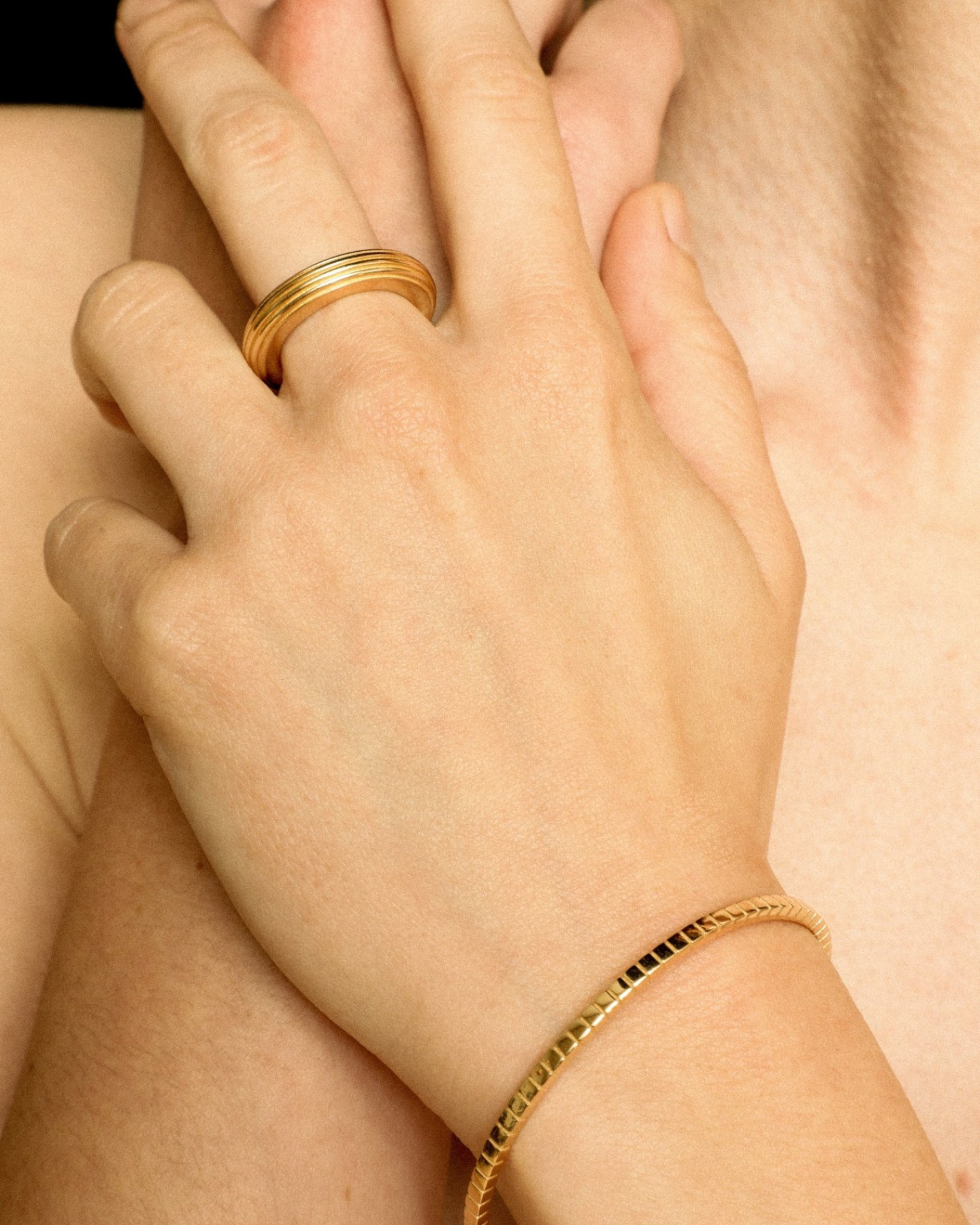 A gold-plated, round-shaped ring with linear engravings worn by a model. 