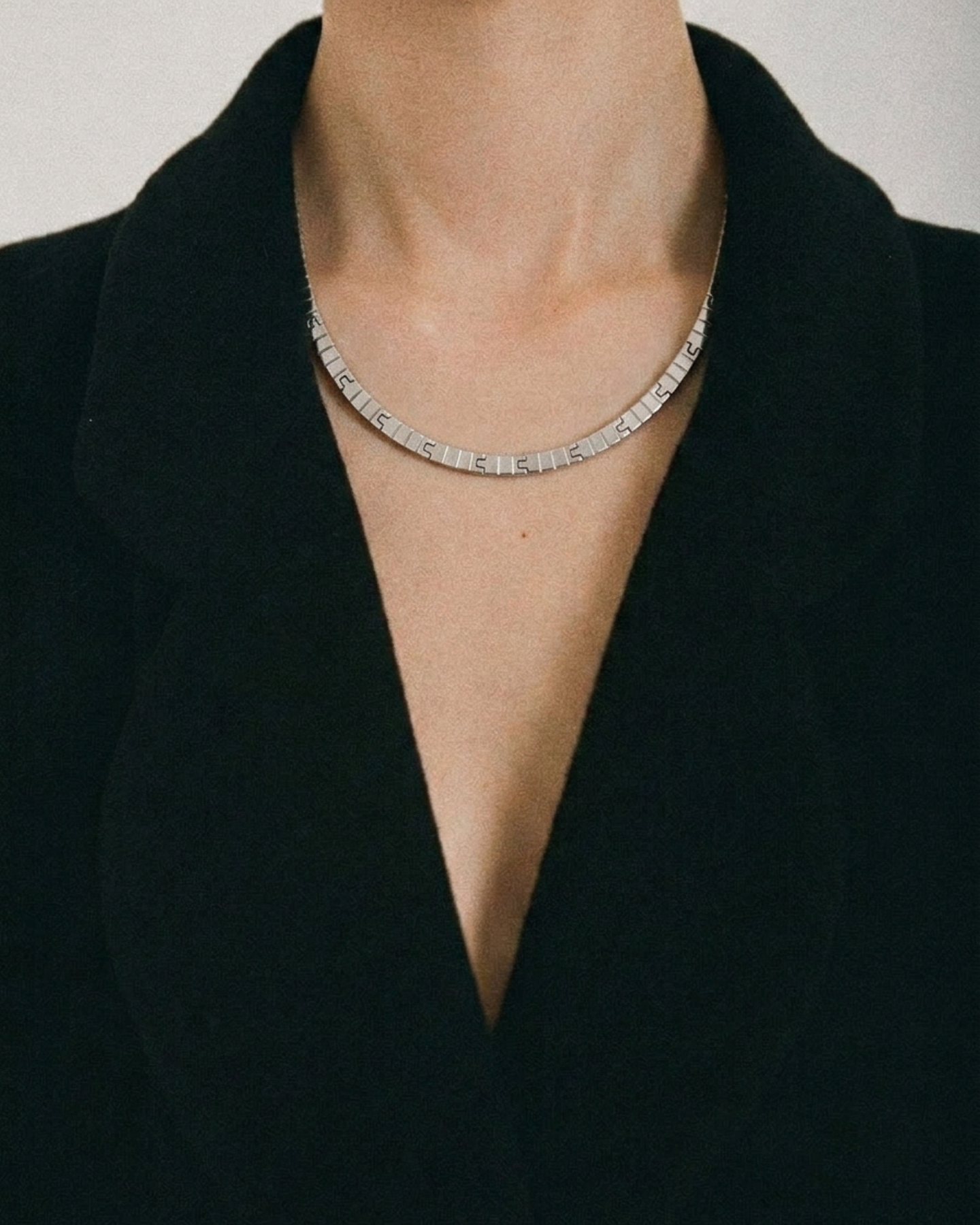 Silver necklace worn by a person in a black outfit against a neutral background