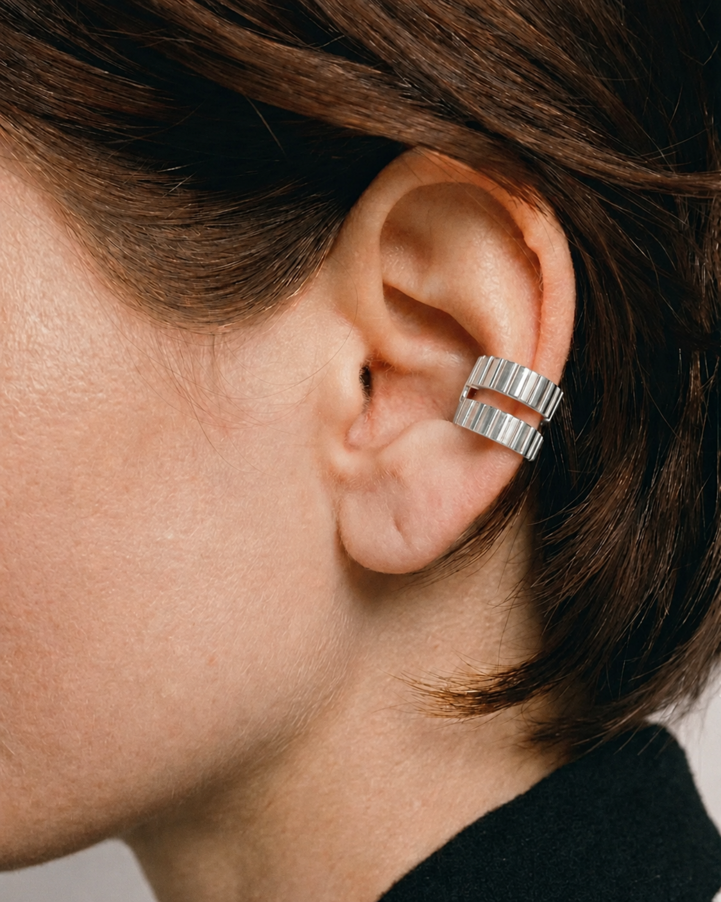 Close-up of an ear wearing a silver ring, with a neutral background