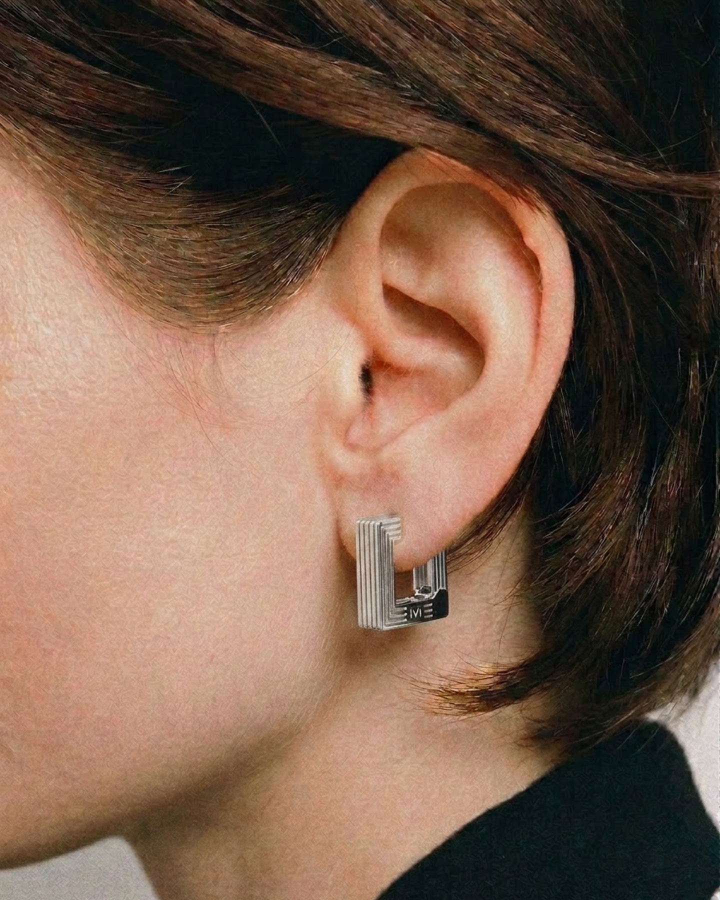 Close-up of an ear wearing a silver earring with a blurred background