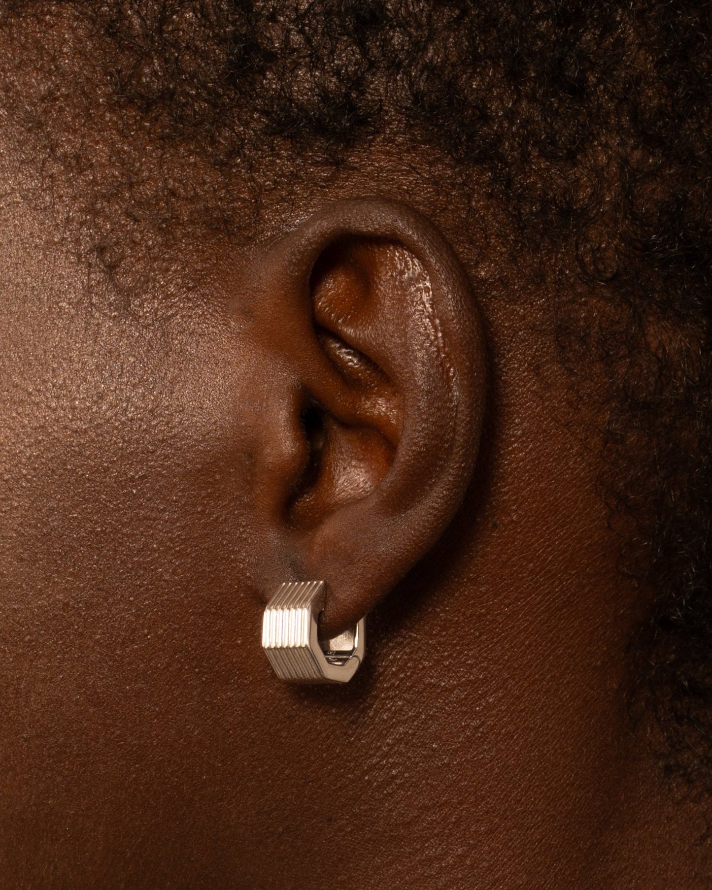 A pair of rhodium-plated wide octagon huggie earrings with a signature angular silhouette, designed to comfortably hug the lobe.
