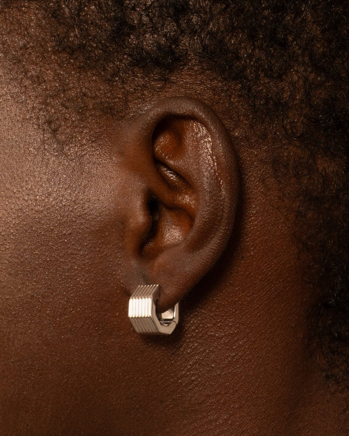 A pair of rhodium-plated wide octagon huggie earrings with a signature angular silhouette, designed to comfortably hug the lobe.