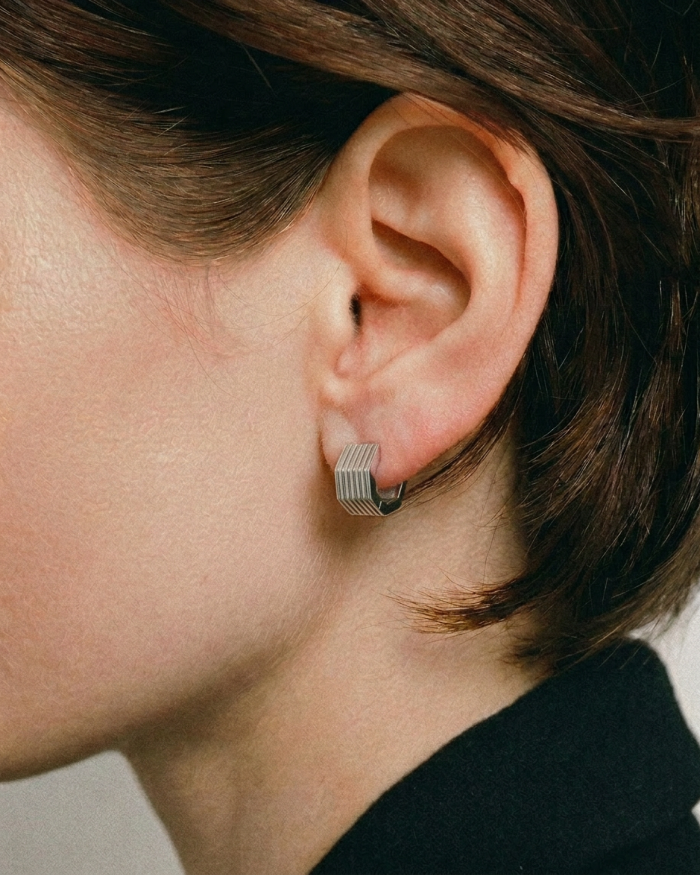 Close-up of an ear wearing a silver hoop earring with a neutral background