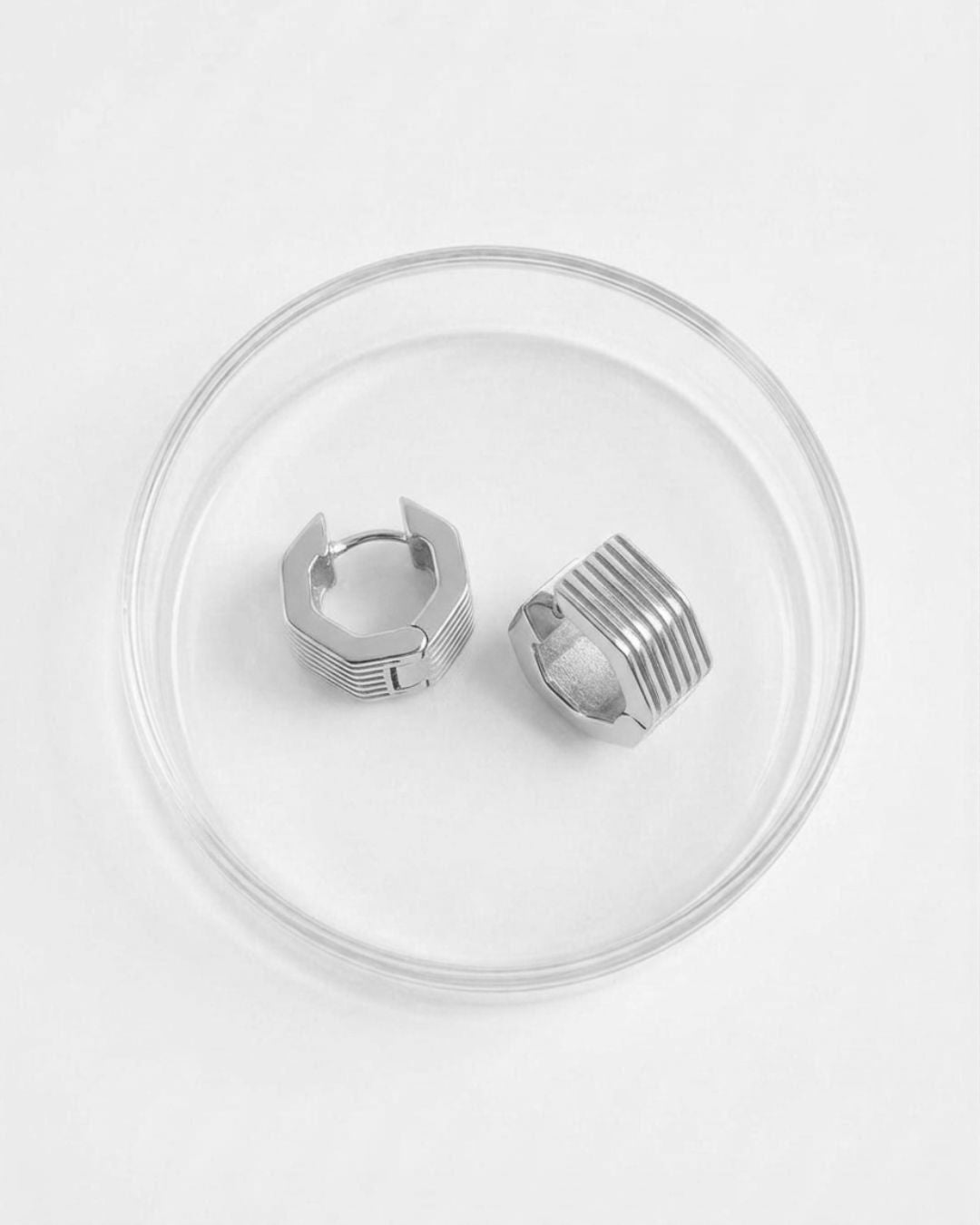 Silver hoop earrings on a clear circular stand against a white background